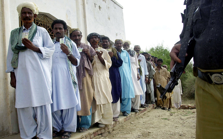 Pakistani men display their identification cards as they stand in a queue to vote in a by-election for a seat in the national parliament, in Tharpakar, Sindh province, 18 August 2004, as policeman stands guard. Shaukat Aziz, the finance wizard chosen by President Pervez Musharraf to be Pakistan's next prime minister, sought to cut a path to the parliament's lower house through a virtually guaranteed by-election in this rural seat. AFP PHOTO/Asif HASSAN